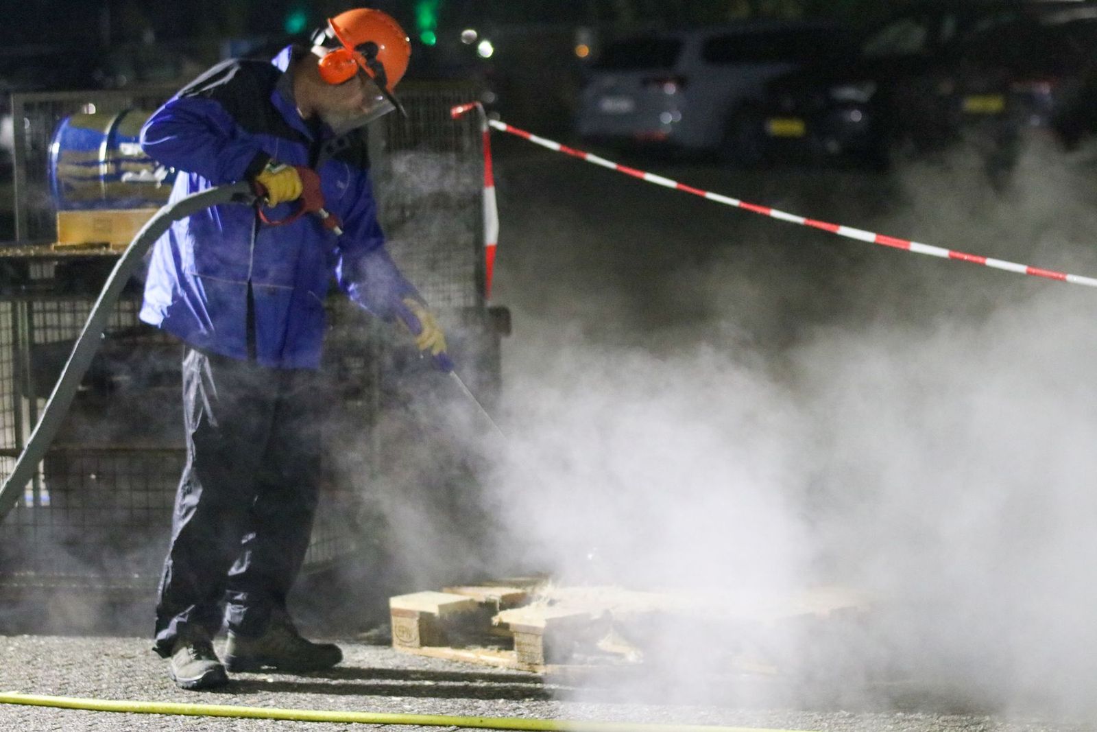 Arbeiter in Schutzkleidung mit Hochdruckreiniger im Wasserdampf